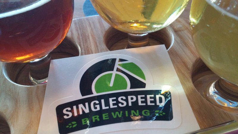Three beers in cups around a black, white and green sticker that says Singlespeed Brewing