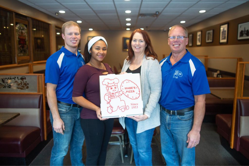 Staff at Mabe's Pizza holding a pizza box that reads "Mabe's Pizza since 1953"