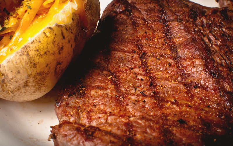 Up-close photo of seasoned steak and a baked potato topped with cheese