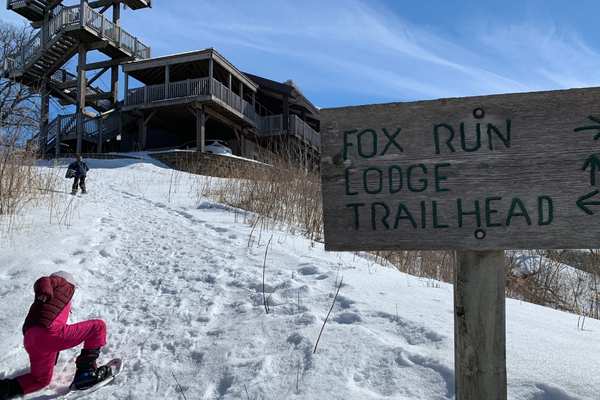 Two kids in snowshoes hike toward the lodge and observation tower at Hitchcock Nature Center 