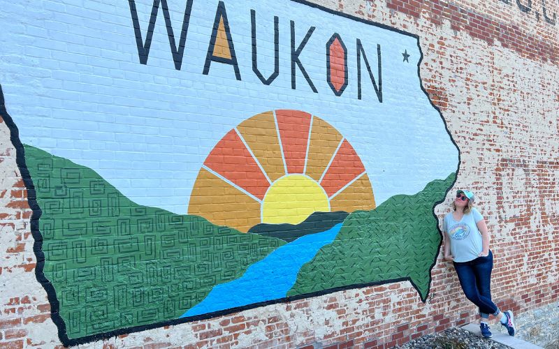Kim in front of a colorful Waukon Iowa mural