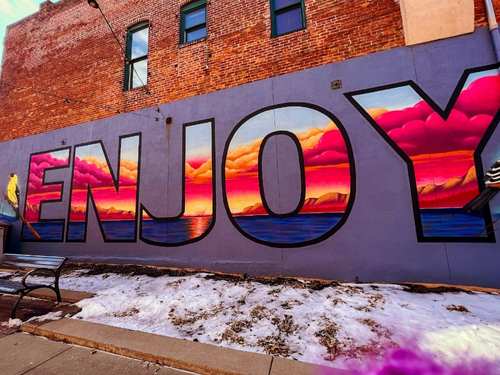 A mural with the word ENJOY painted on it with a sunset in the letters. Mural is found in downtown Council Bluffs, Iowa.