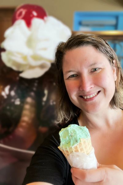 Kim with her pistachio ice cream waffle cone with a giant ice cream sundae behind her