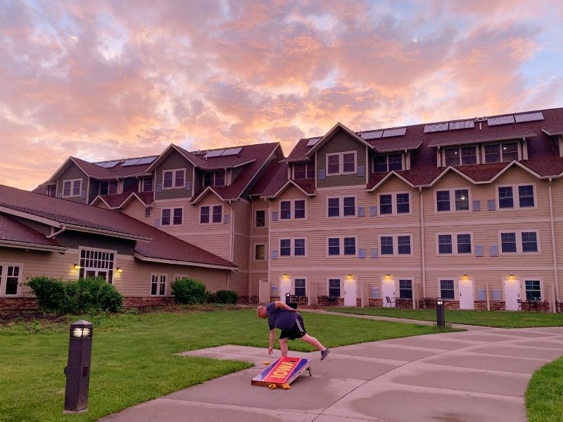 The exterior of Honey Creek Resort at dusk, with a man by a corn hole game 