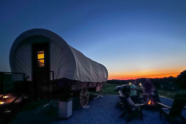 A family sits near the campfire next to a covered wagon at Best Nest Farm in Glenwood