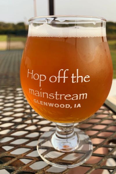 A glass of beer with the words "Hop off the mainstream. Glenwood, Iowa" on it