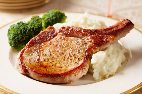 A pork chop served on top of mashed potatoes with a side of broccoli