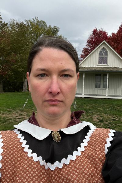 Kim posing in a costume in front of the American Gothic House