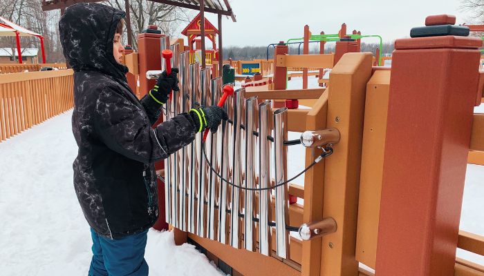 A boy in winter gear plays an instrument in the snow at the Dream Playground located at Lake Manawa State Park